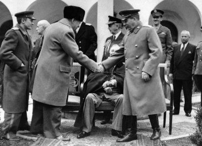 Иосиф Сталин (справа) и премьер-министр Великобритании Уинстон Черчилль пожимают друг другу руки на территории Ливадийского дворца. Сидит американский президент Франклин Д. Рузвельт. За президентом стоит адмирал Уильям Лихи.